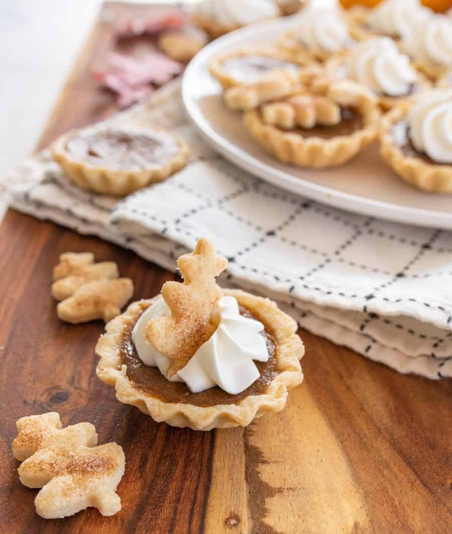 A mini pumpkin pie with a whipped cream swirl and a pie crust cookie dusted with cinnamon sugar on top.