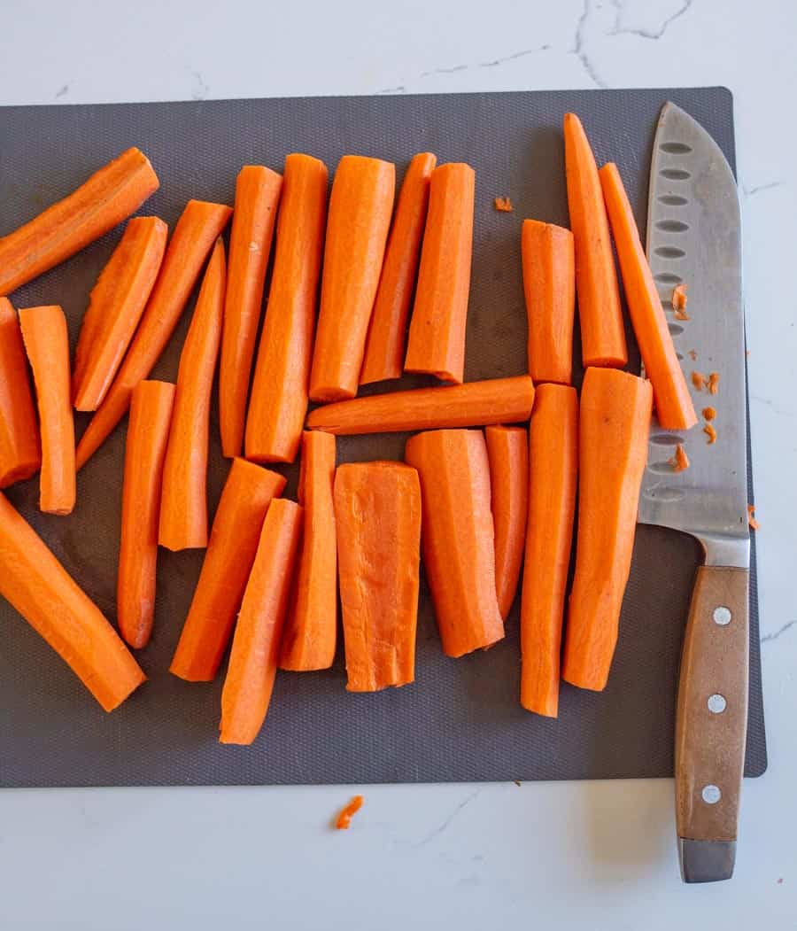 Raw carrots on a grey cutting board with a chef's knife with a wooden handle.