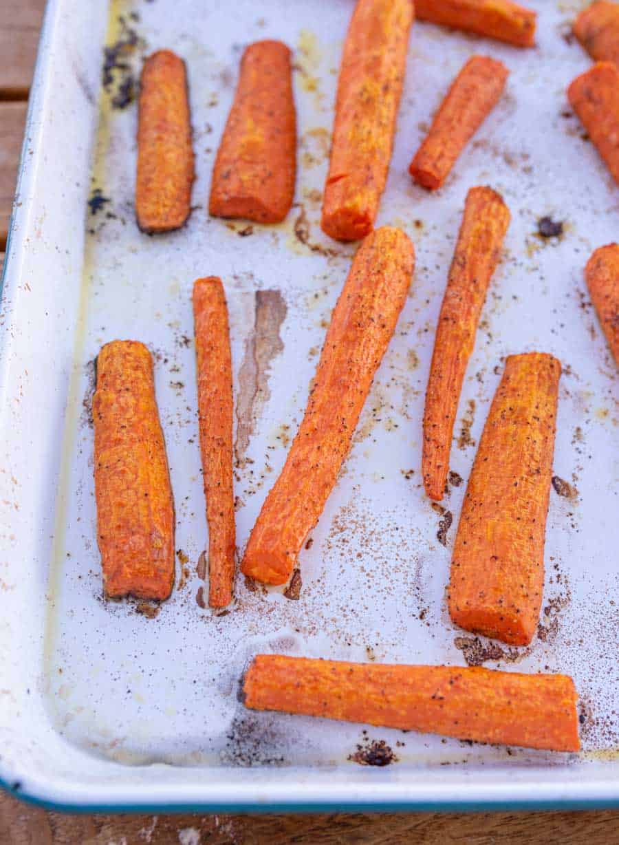 Roasted carrots on a white enamel pan after roasting.