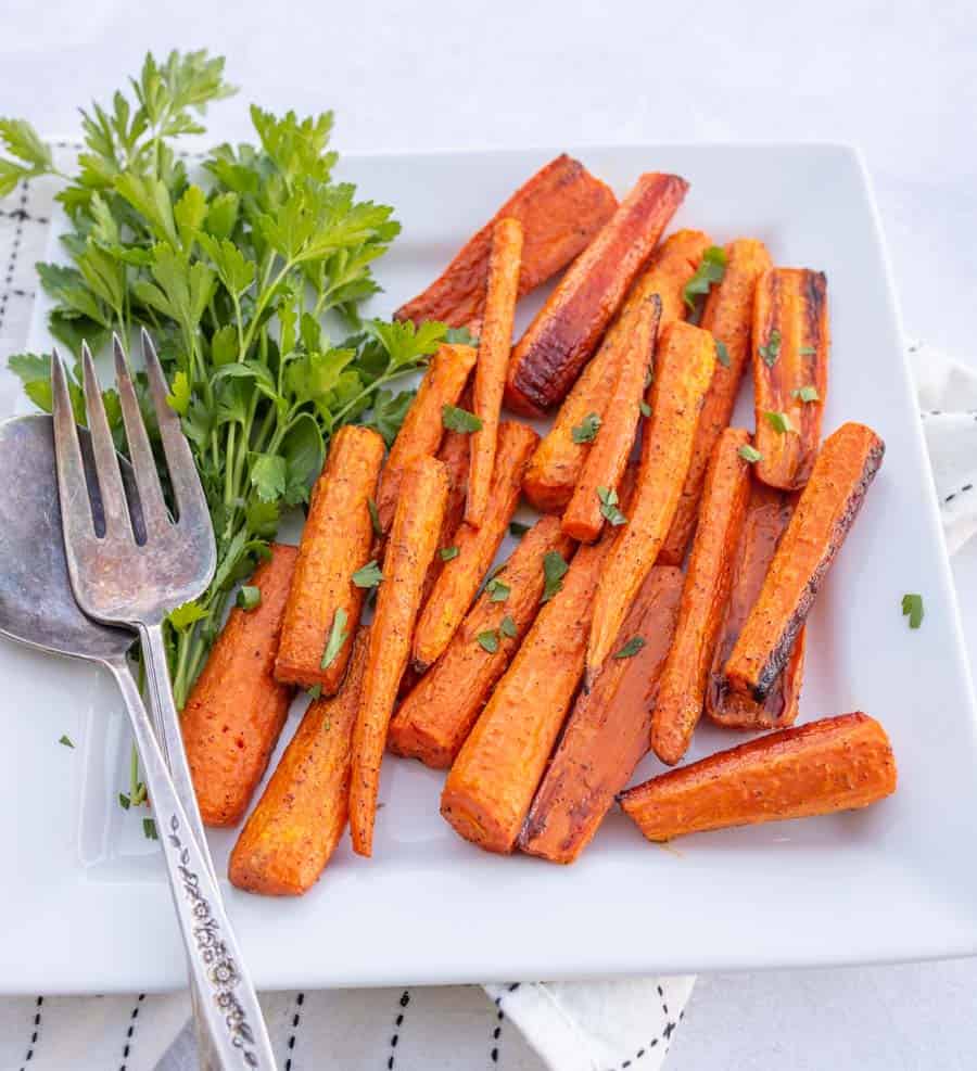 Roasted carrots on a white plate with a fork and spoon.