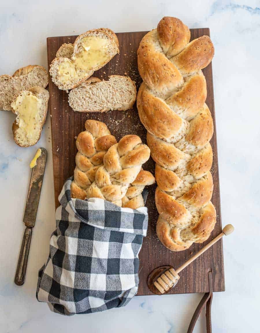 4 loaves of bread bread on a dark wood cutting board, one wrapped in a black and white checkered cloth.
