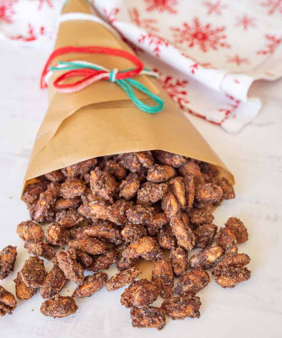 Cinnamon candied almonds spilling out of brown bag tied with some red, green, and white yarn.