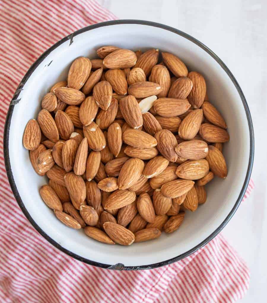 A white bowl with a black rim filled with raw almonds.