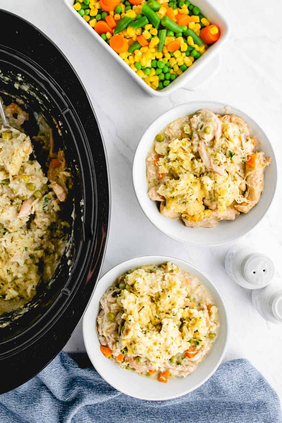 Two white bowls that contain chicken stew next to a crockpot with chicken stew.