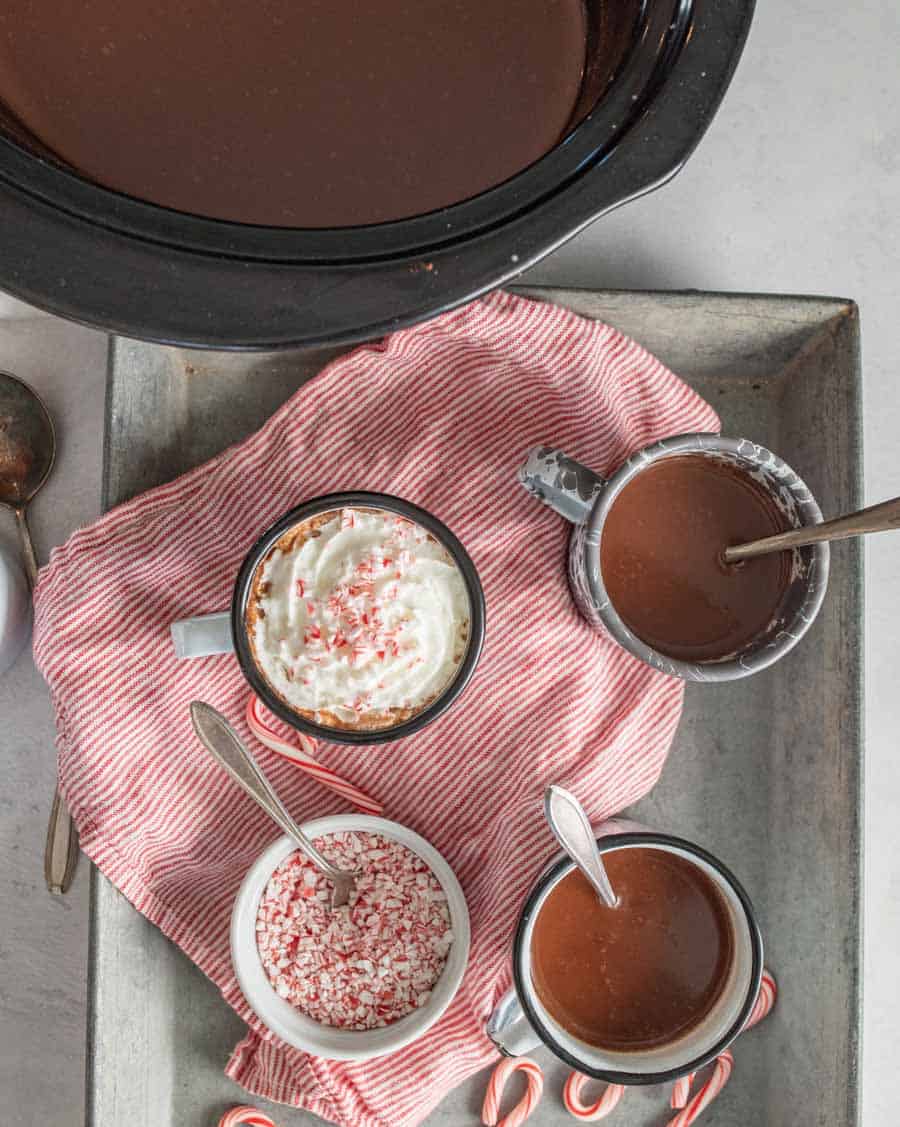 Top view of mugs filled with crock pot hot chocolate with spoons and a ramekin of of crushed candy canes next to them.