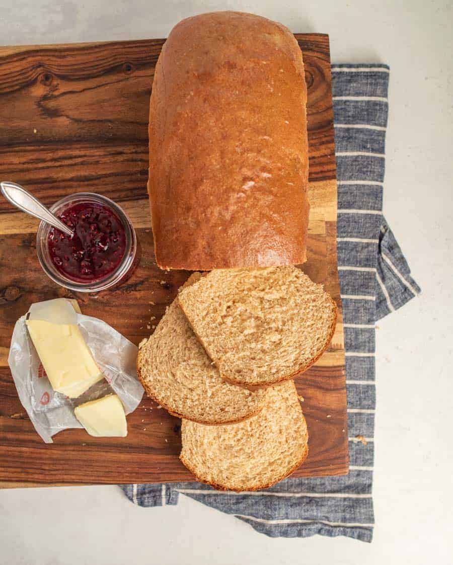 a whole wheat bread loaf with three slices cut with butter and jam next to it.