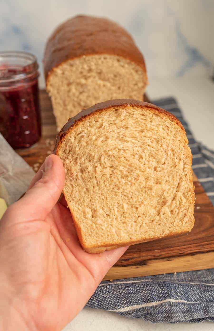 hand holding a slice of whole wheat sandwich bread.
