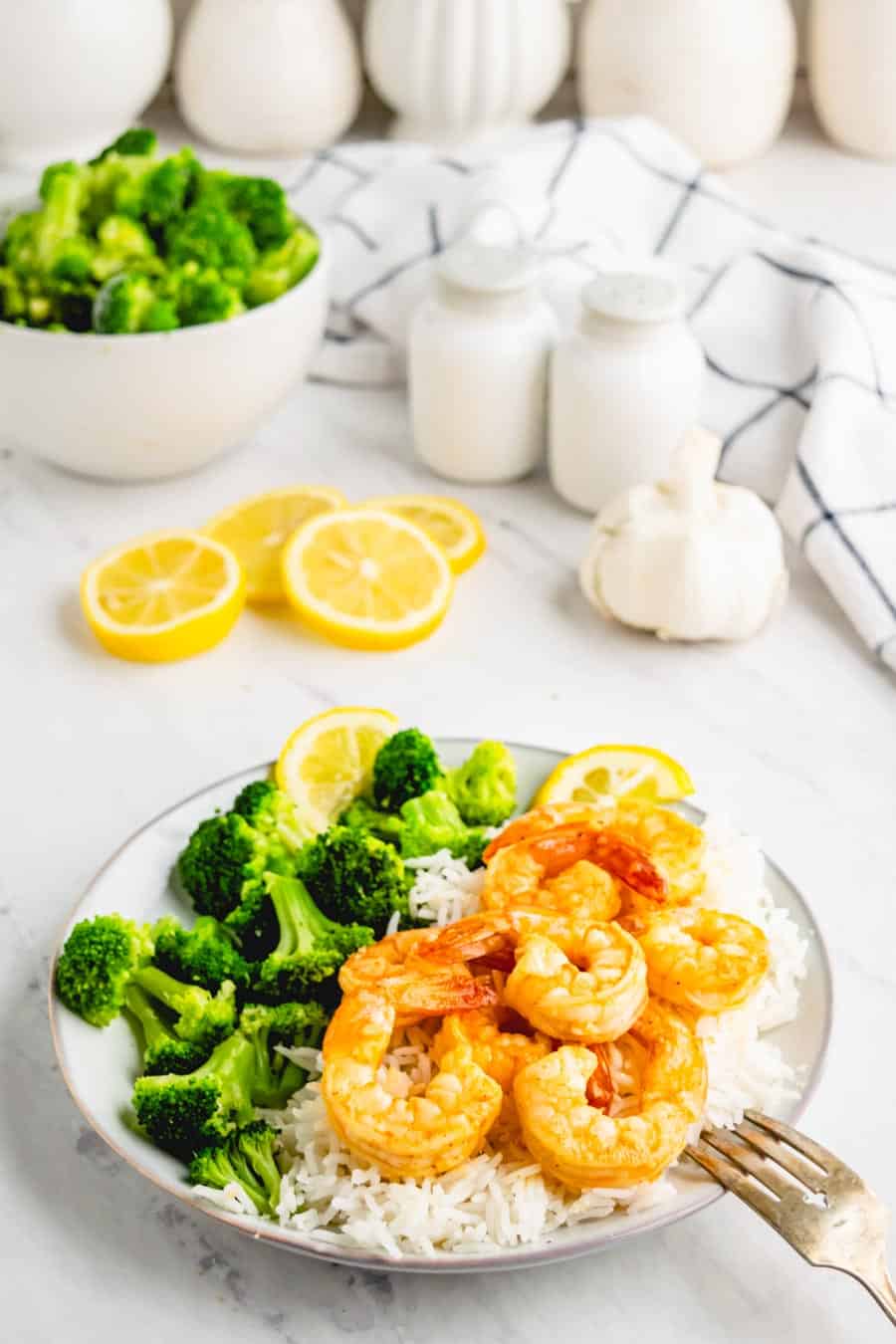Light grey plate with cooked garlic shrimp over white rice and broccoli to the side.