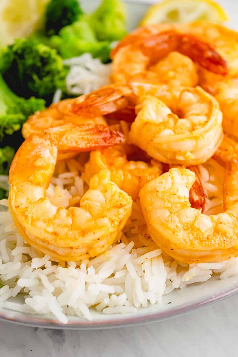 Several cooked garlic shrimp on top of white rice and next to some steamed broccoli.