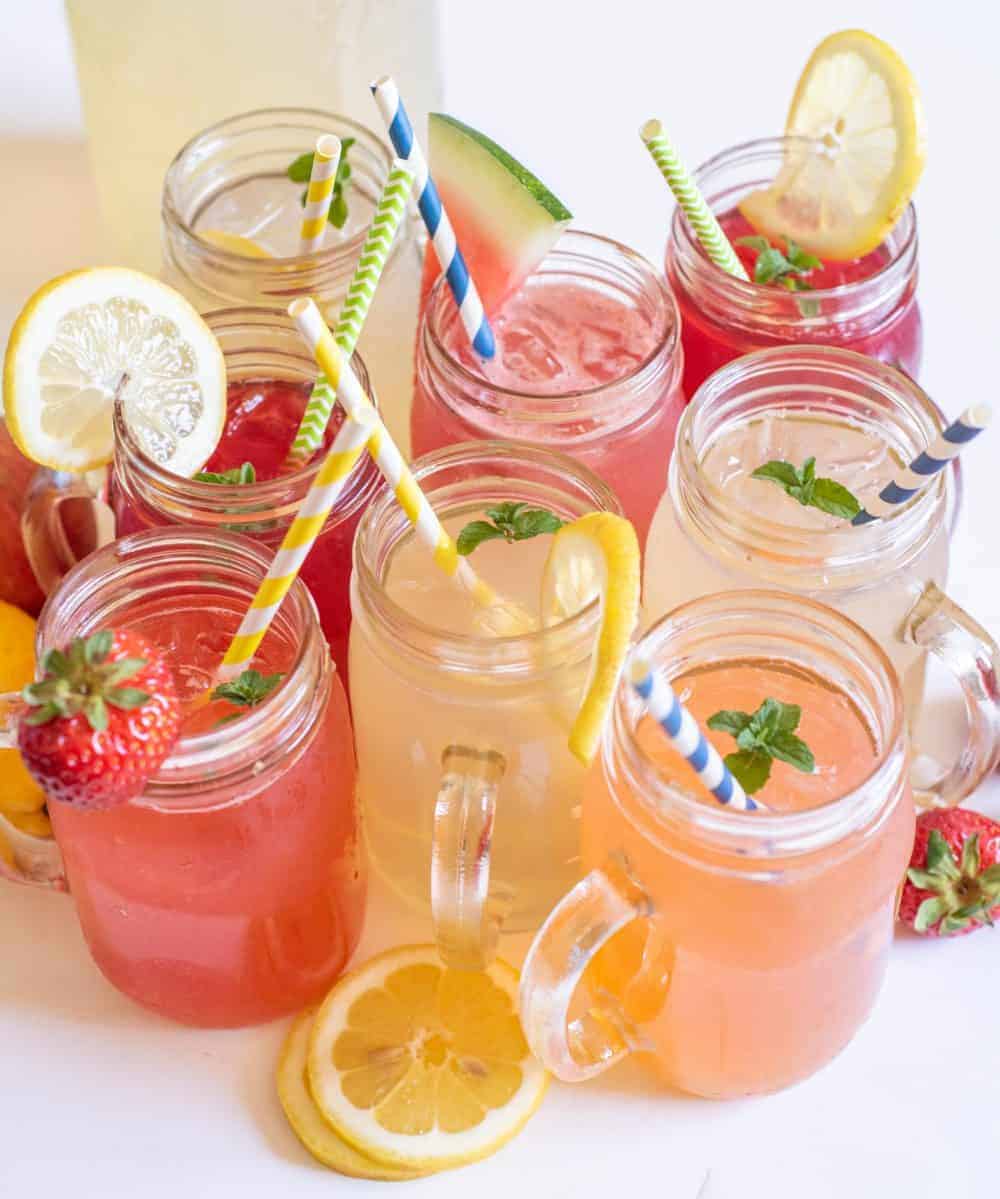 Glass mugs filled with different types of lemonade with straws in them.
