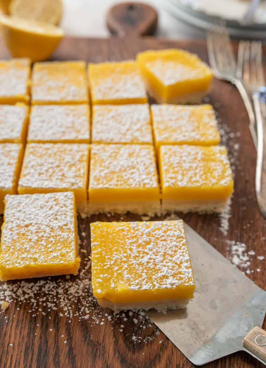 Lemon bars sprinkled with powdered sugar with one bar being removed by a thin metal spatula.