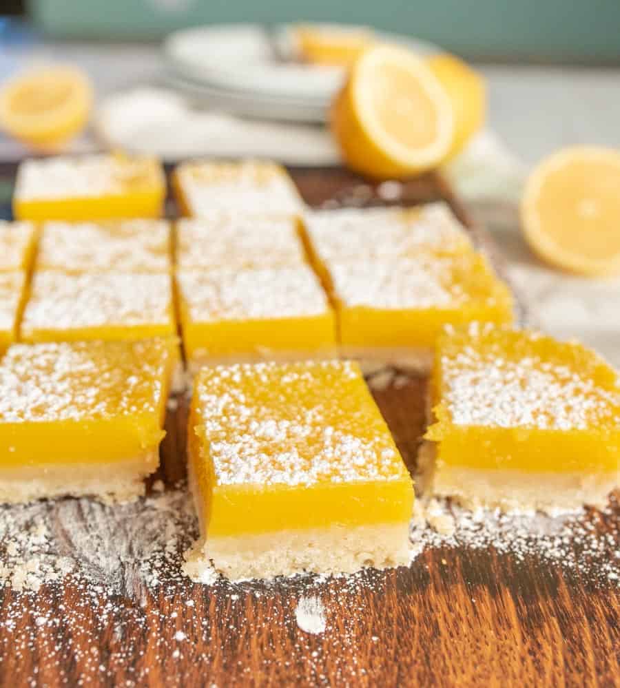 Cut lemon bars sprinkled with powdered sugar on a wooden cutting board.