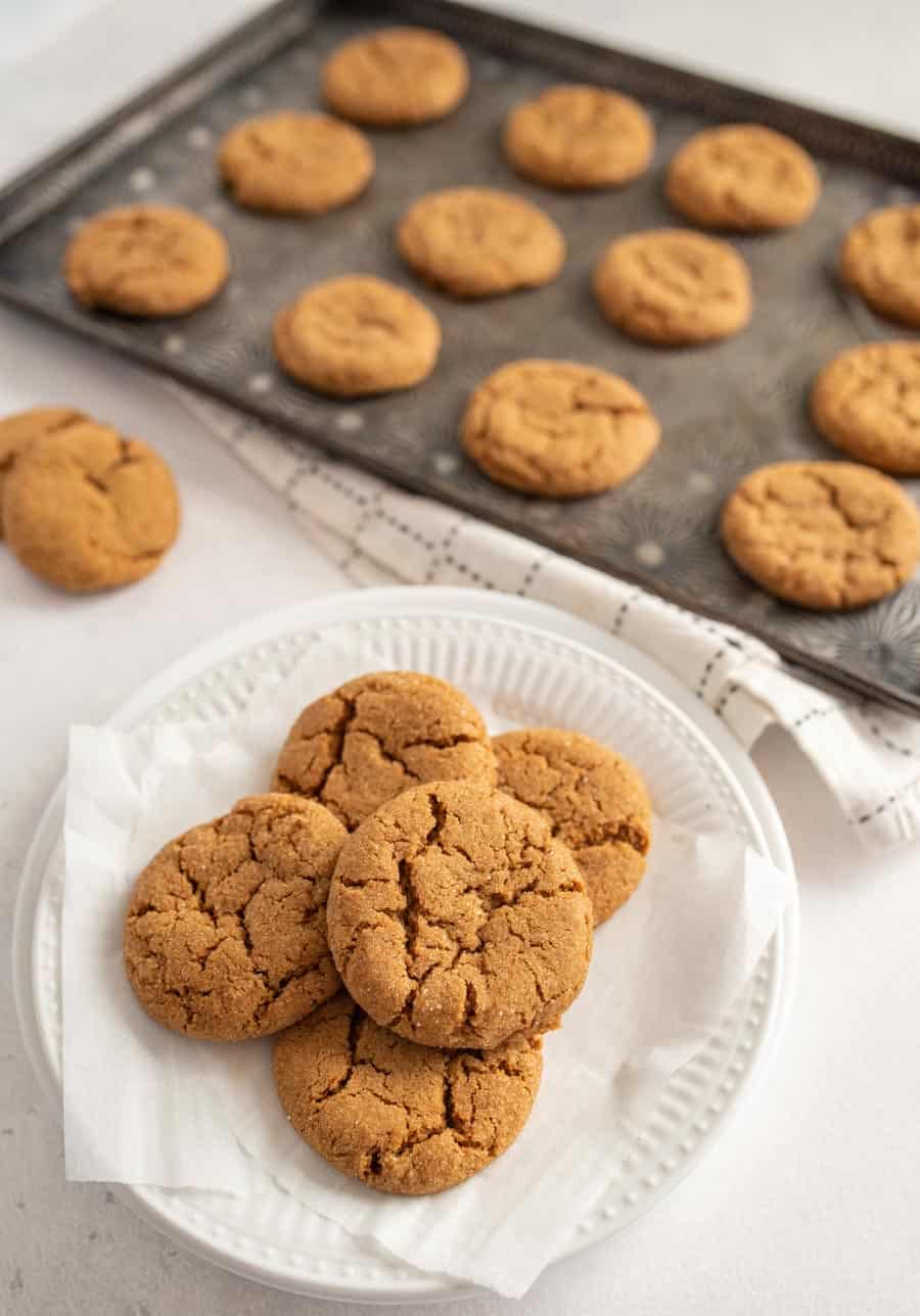 Five old fashioned molasses cookies on a white plate with a dozen molasses cookies on a baking sheet in the background.