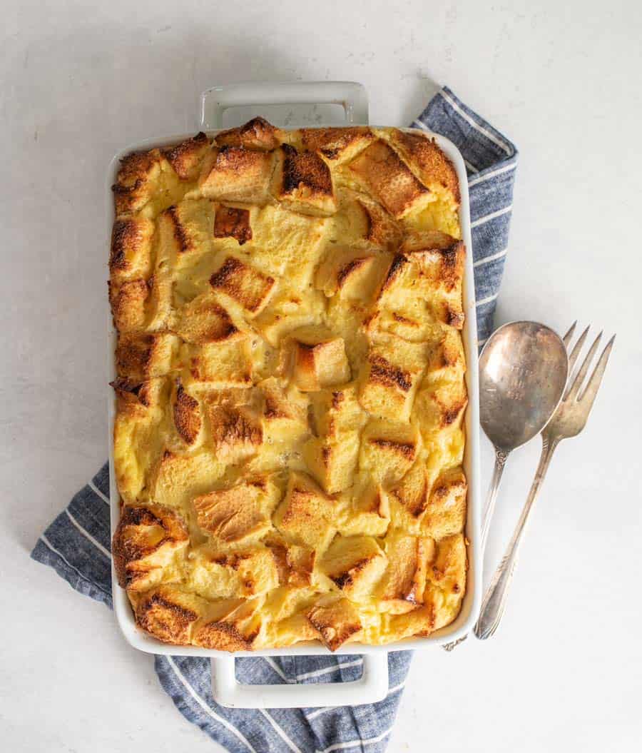 Top view of French toast breakfast casserole in a white baking dish with serving utensils next to it.