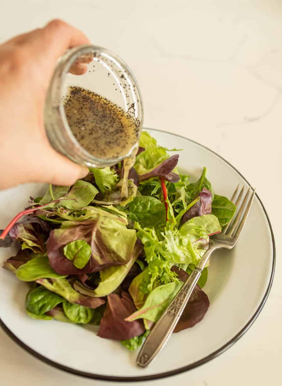 hand pouring salad dressing over a plate of salad featuring easy salad dressing recipes.