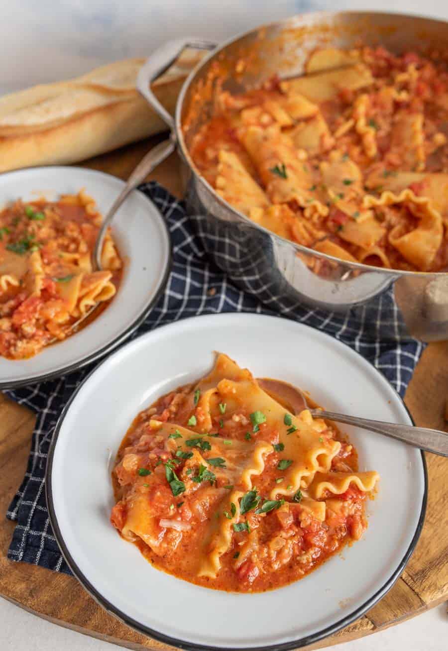 Lasagna soup in white bowls with parsley on top next to a pot of lasagna soup.