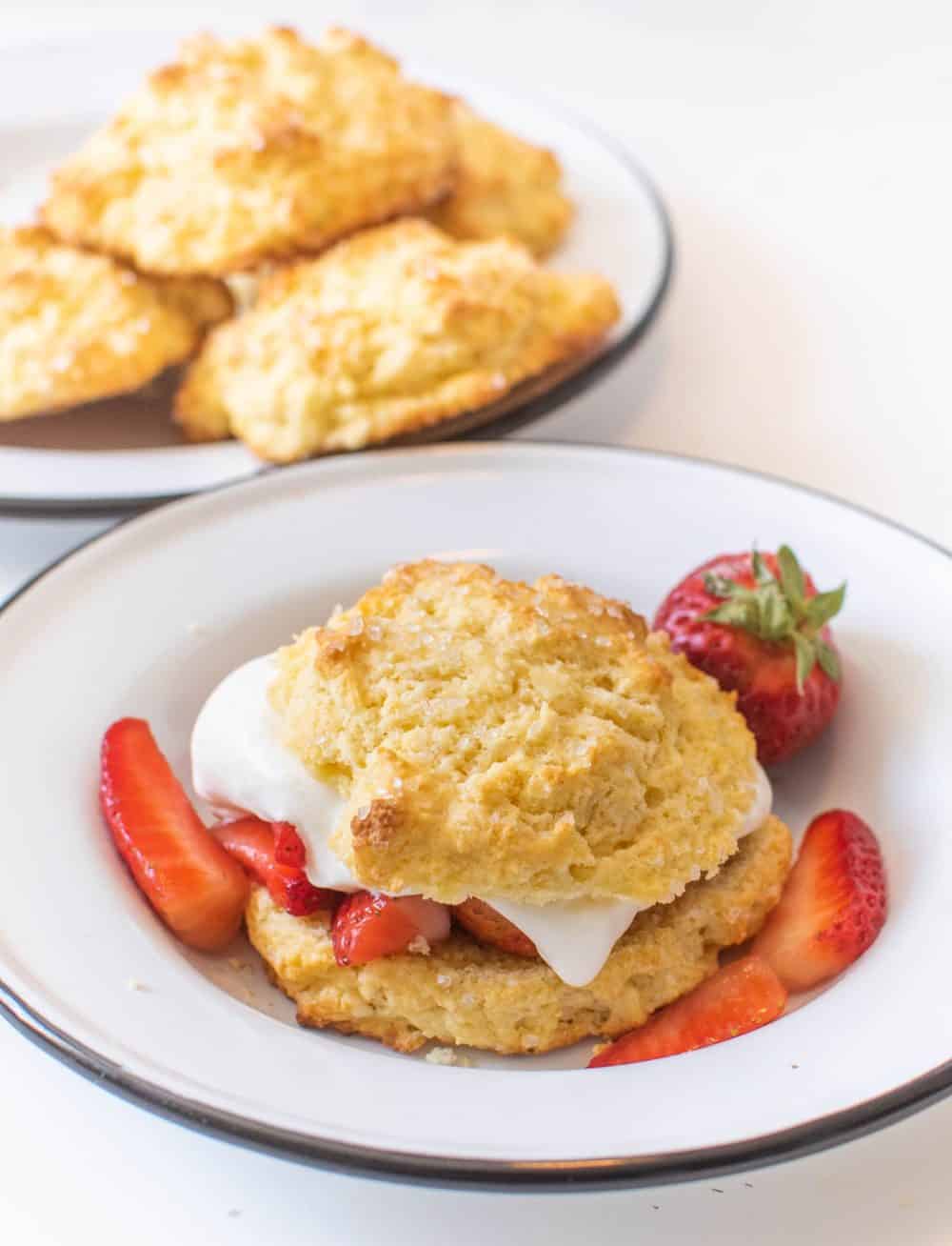 A bowl with a strawberry short cake biscuit, whipped cream, and sliced strawberries featuring a biscuit recipe for strawberry shortcake.