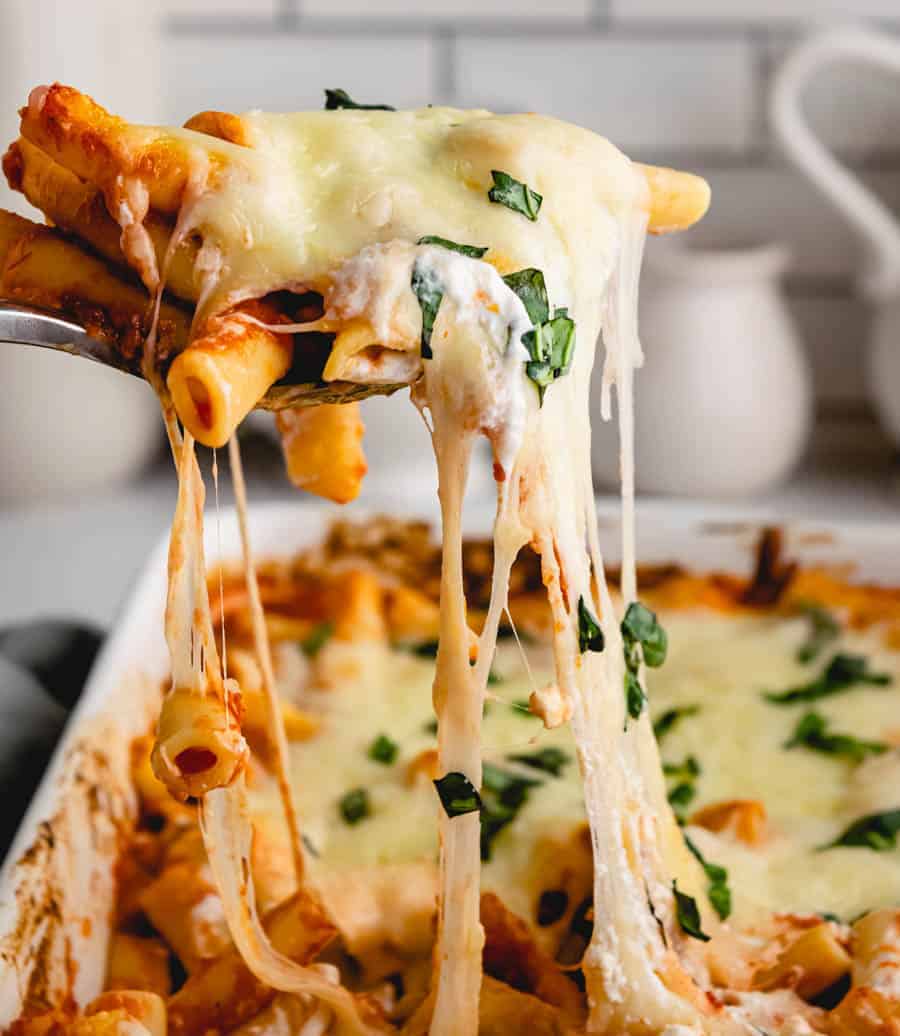 Baked ziti being scooped out of baking dish with a cheese pull.