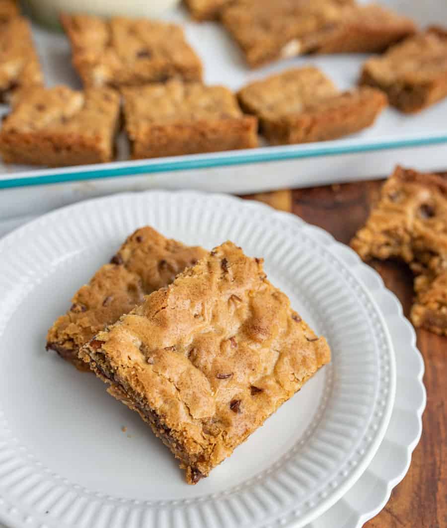 A close up of a plate of blondies with a pan of blondies in the background.