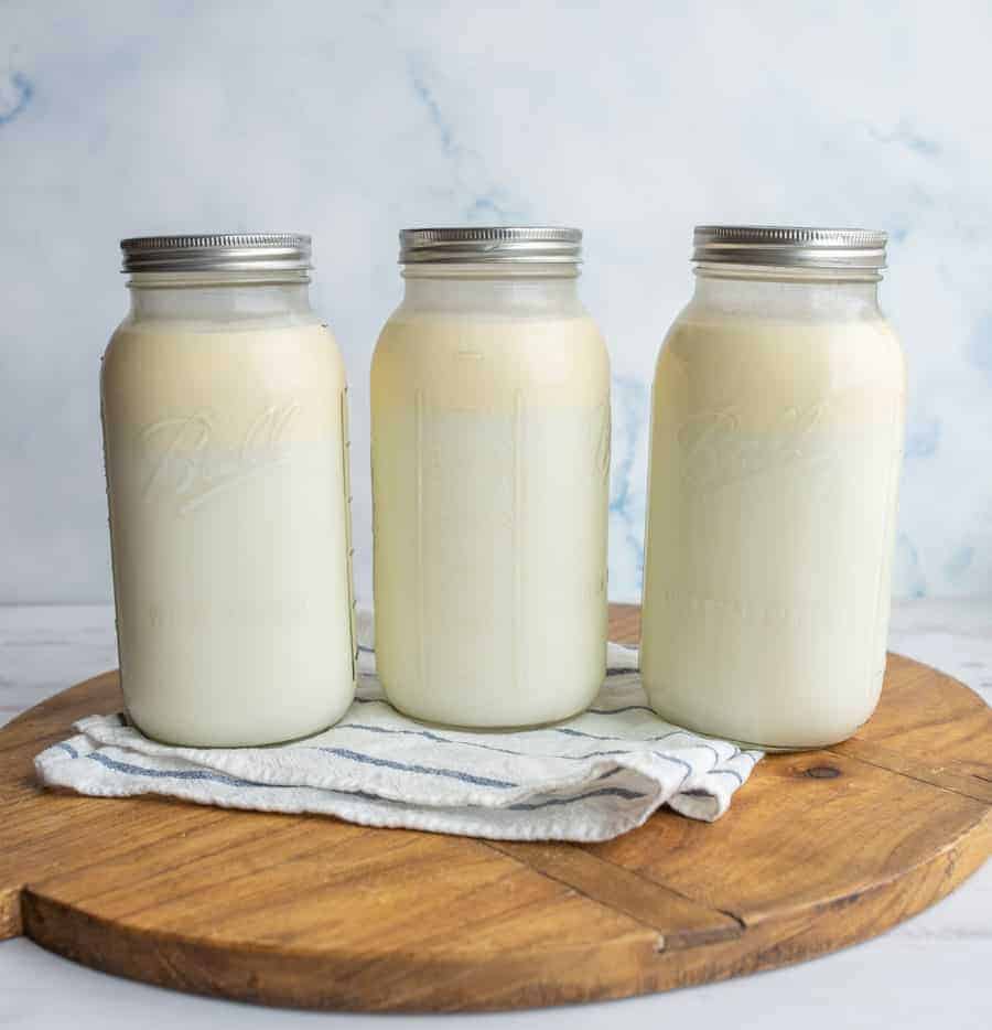 Three glass jars of buttermilk on a white napkin and wood cutting board.