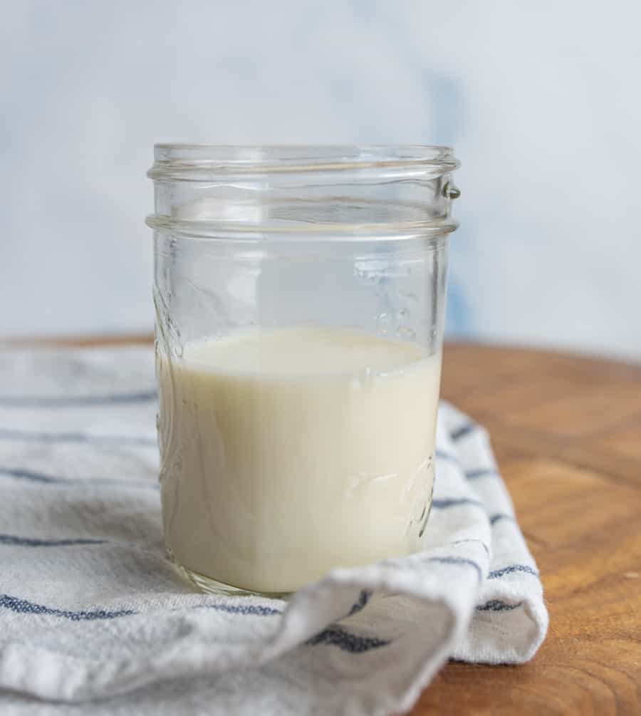 A close up of a glass of buttermilk on a white linen.