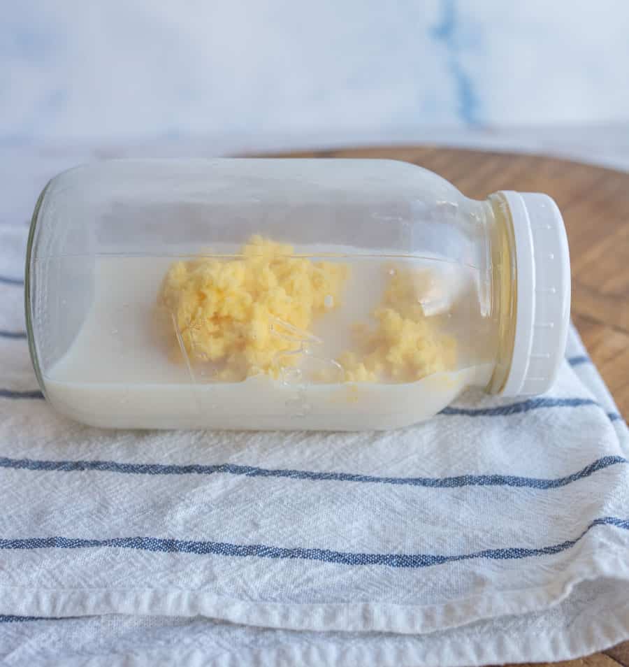 A glass jar on its side with butter and buttermilk inside on a white napkin with blue stripes.