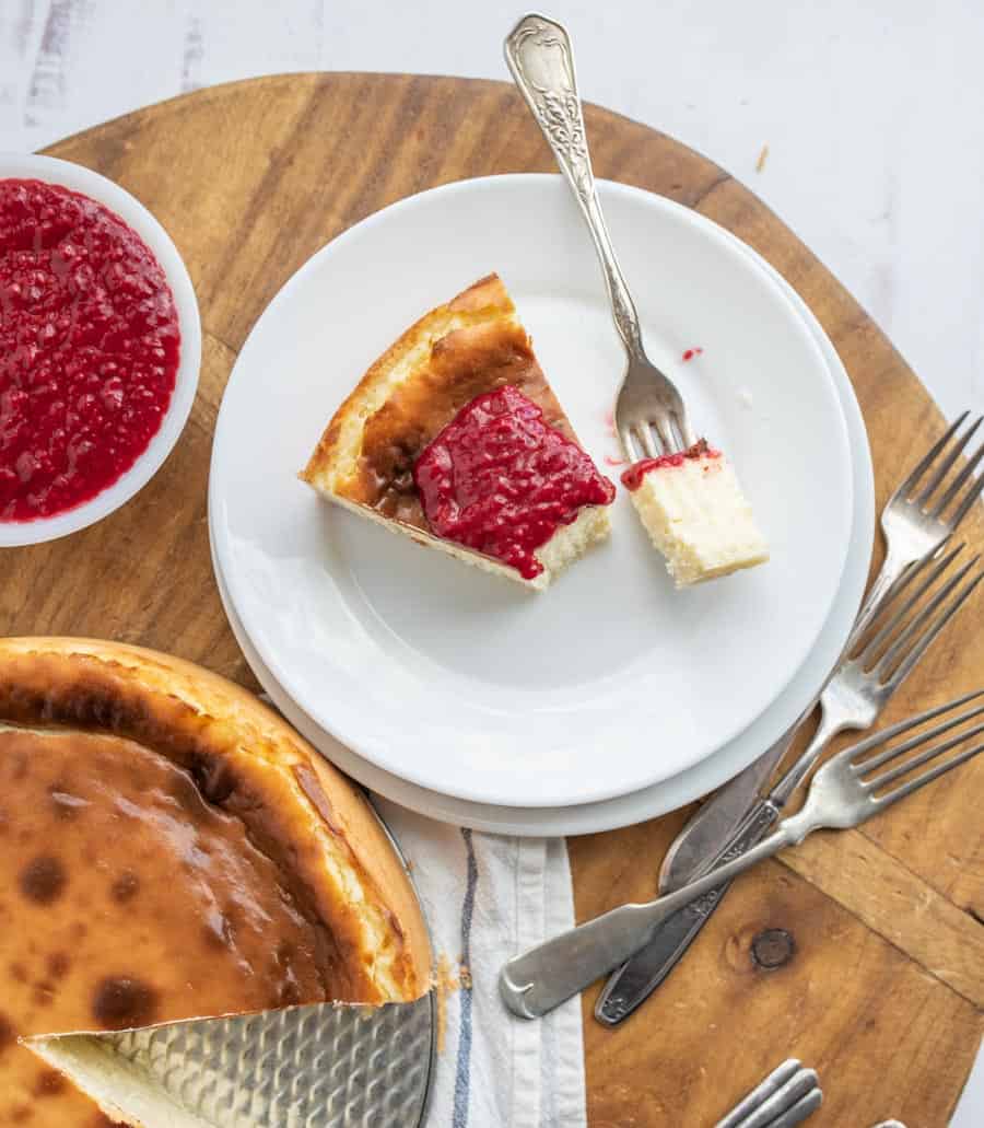 Top view of a slice of cheesecake with a bite sitting on a fork next too the full cheesecake with a slice taken out.