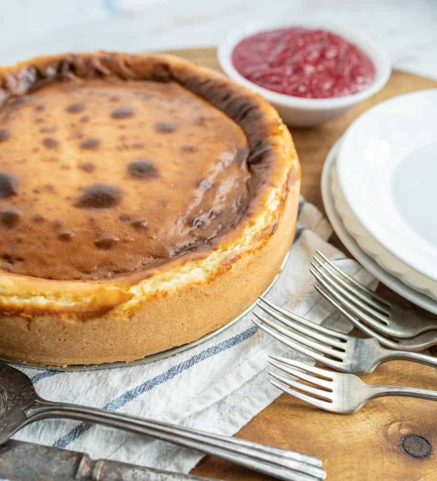 An uncut cheesecake next to plates and forks.