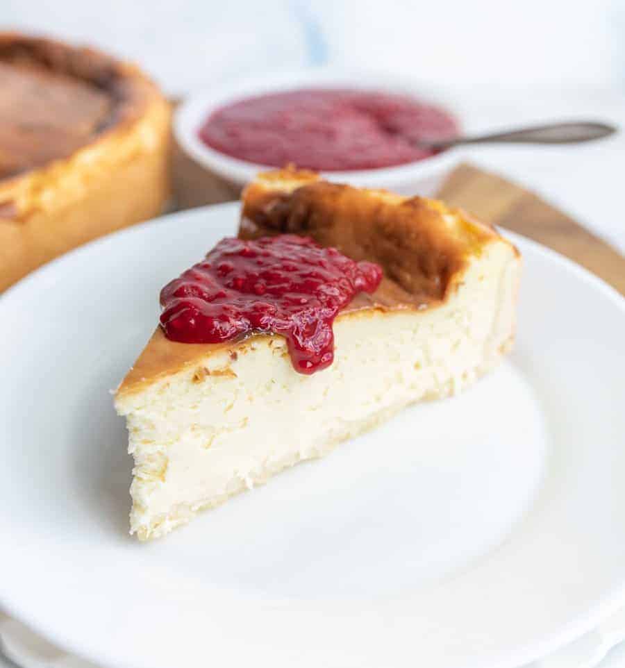 A close up of a slice of cheesecake on a white plate with a dollop of raspberry sauce dripping off the top.