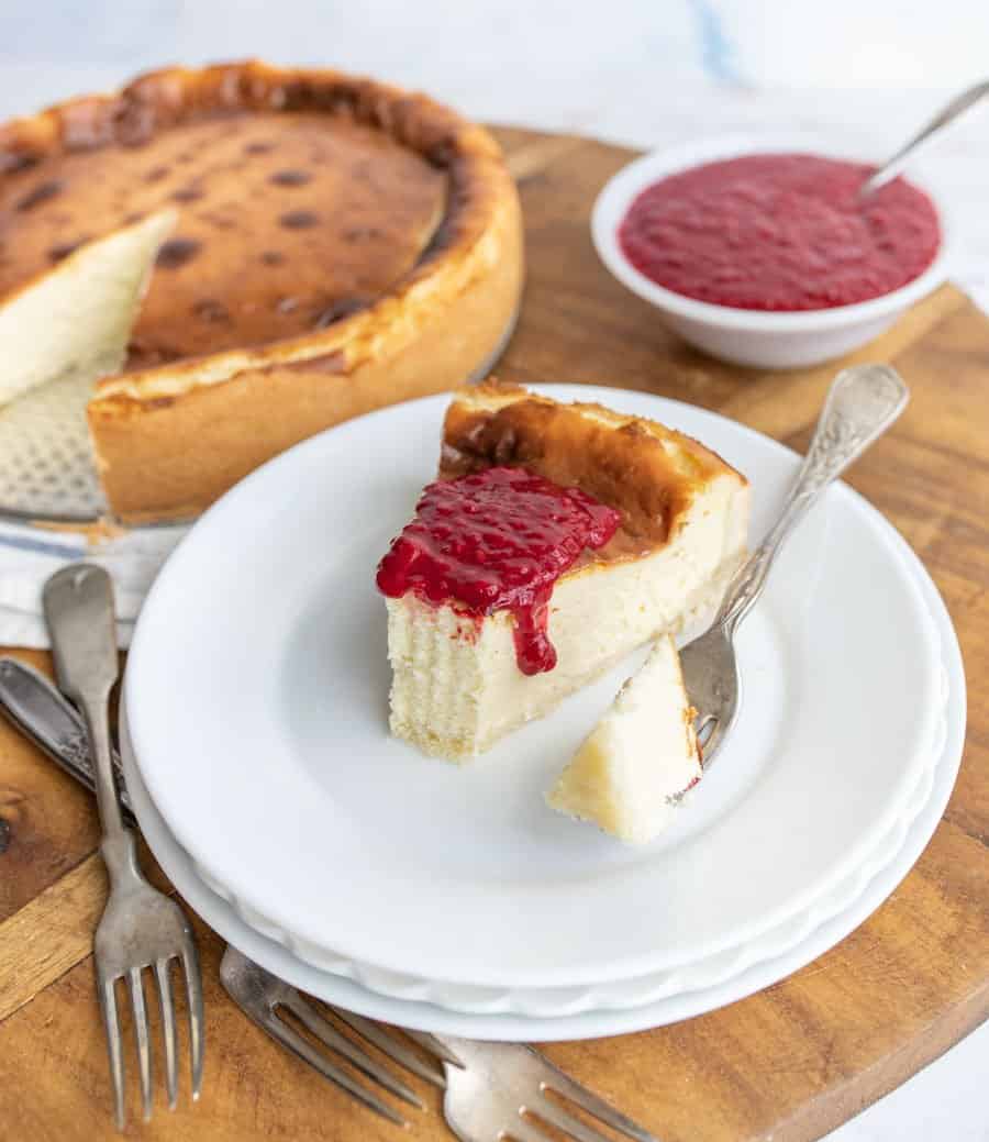 A slice of cheesecake topped with raspberry sauce on a plate with the cheesecake in the background.