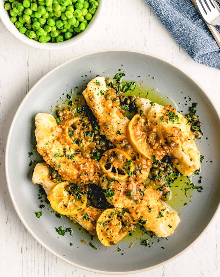 A top view of a plate of chicken picatta with lemon slices.