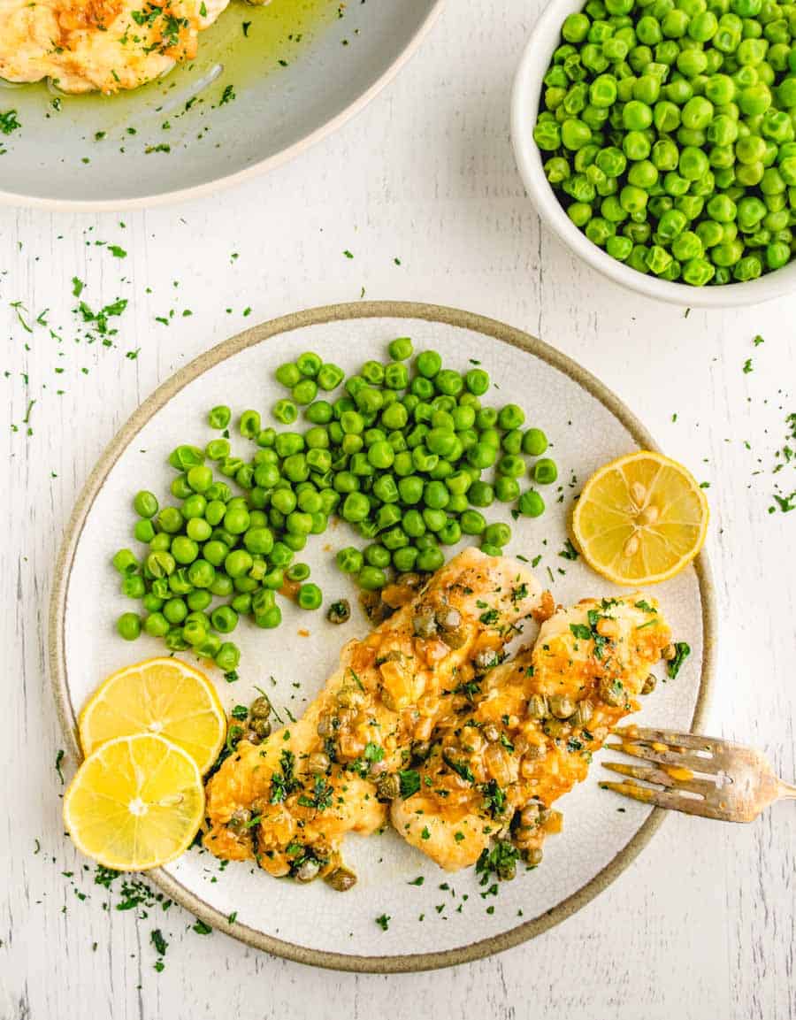 A plate of chicken picatta with lemon slices and a side of peas.