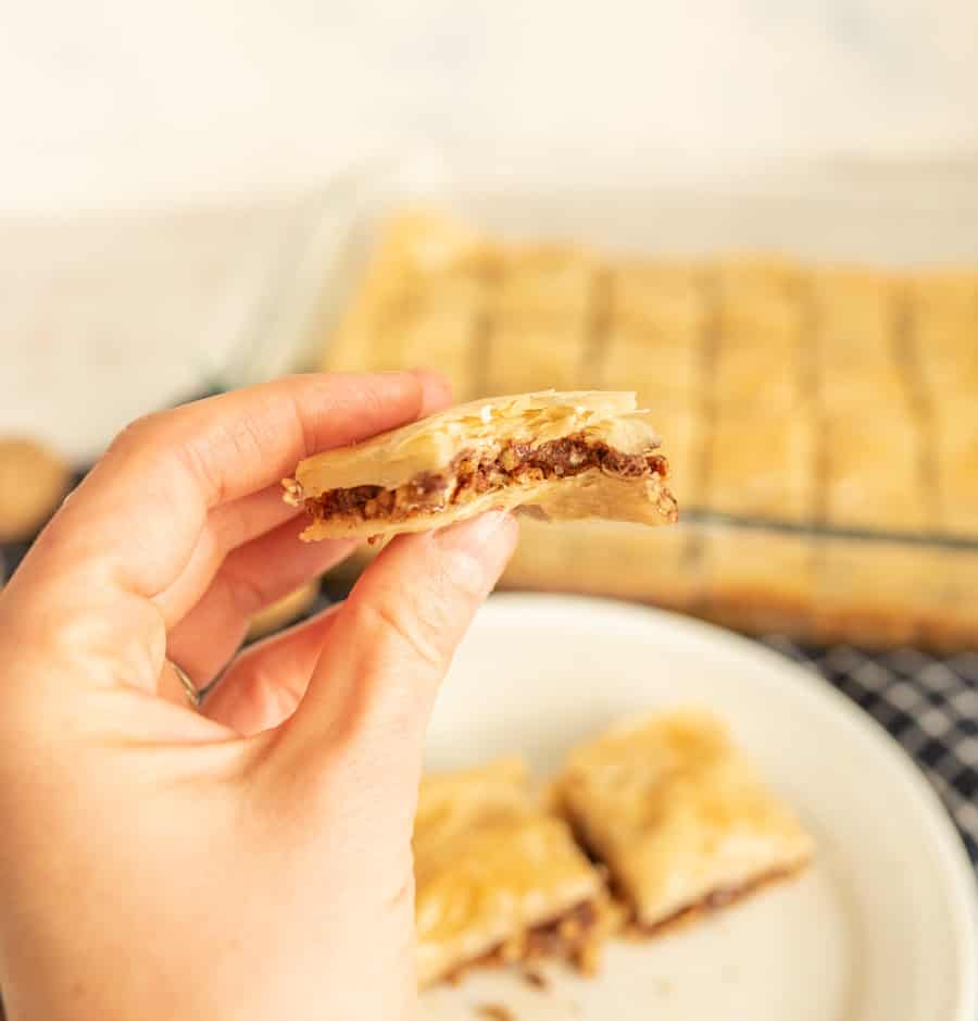 A close up of a hand holding a piece of baklava.