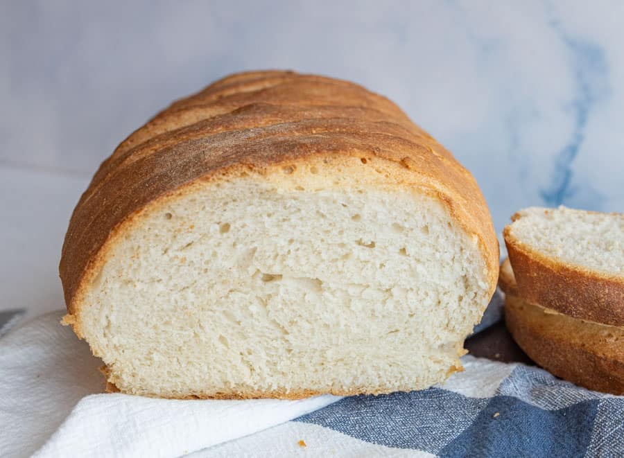 Close up of a loaf of Italian bread that has been cut into resting on a blue and white towel.