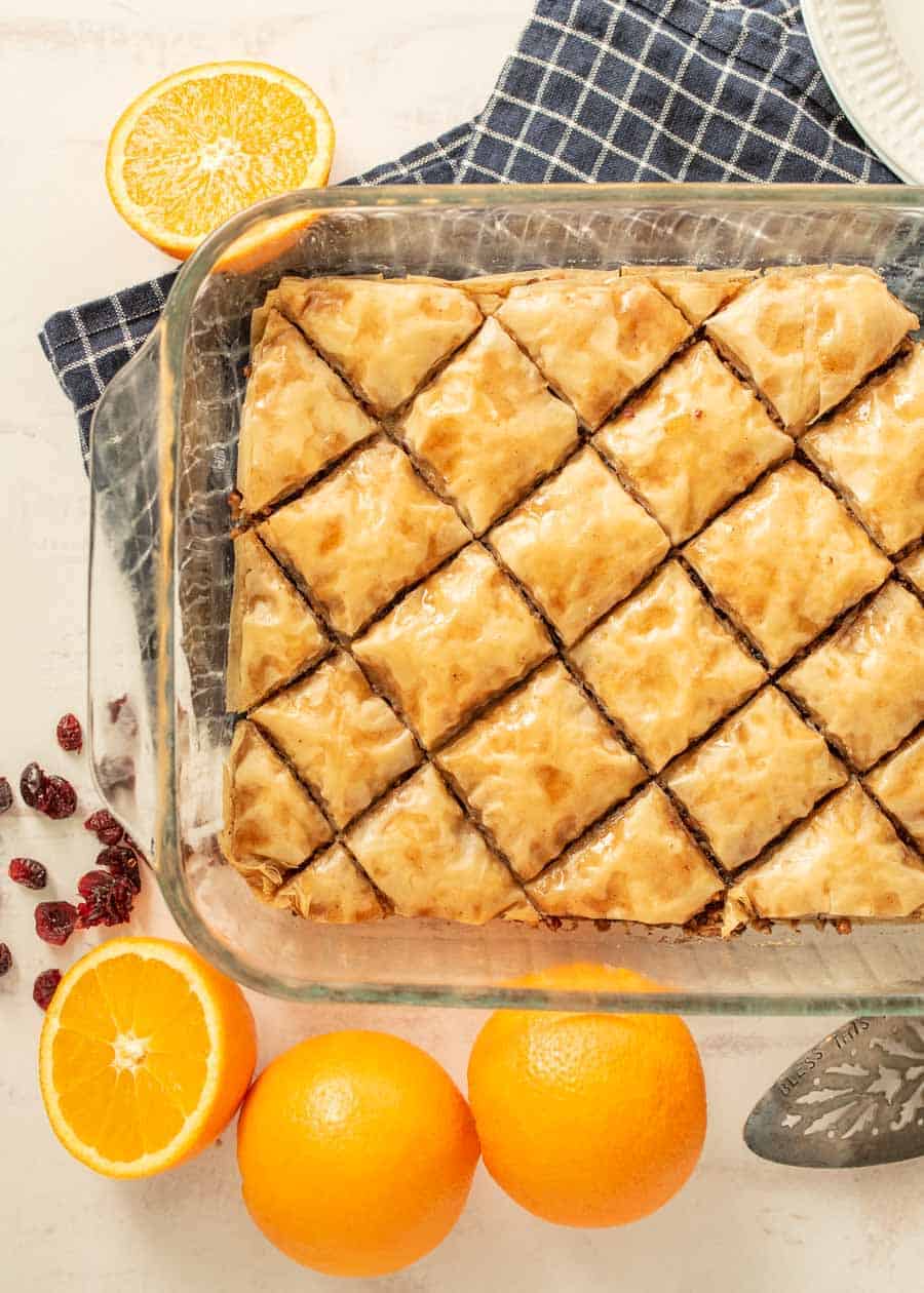 Top view of baklava in a pan with oranges and cranberries around the dish.