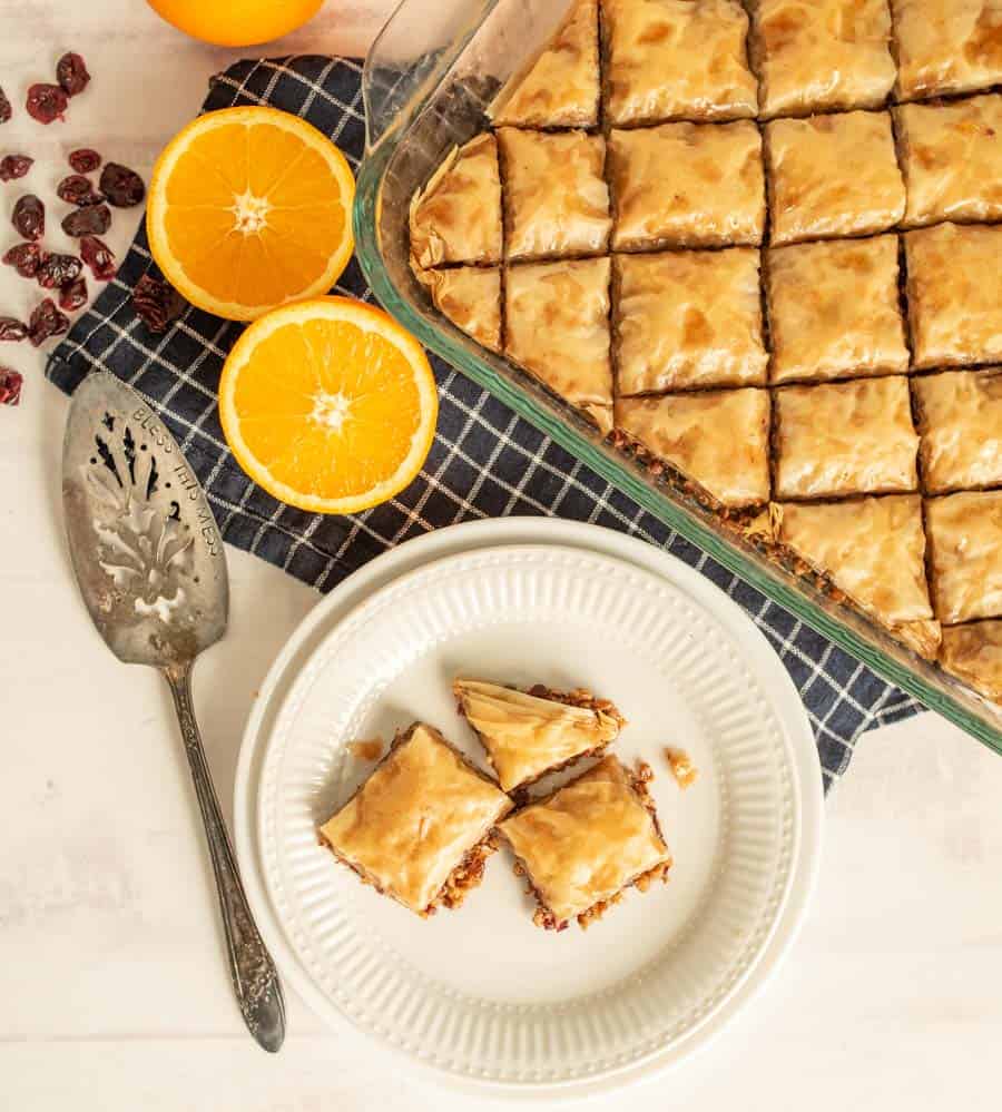 A top view of a plate and pan of baklava with oranges and cranberries next to it.