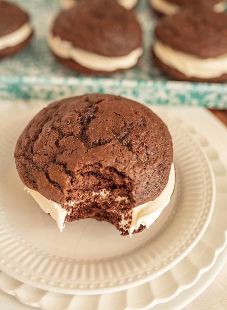 A close up of a whoopie pie with a bite taken out of it on a white plate.