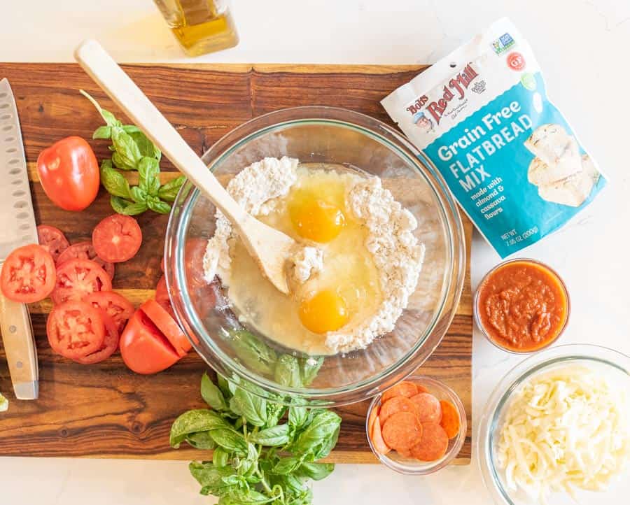 A top view of Grain-free flatbread mix bag, and bowls of the other ingredients for the gluten-free pizza.