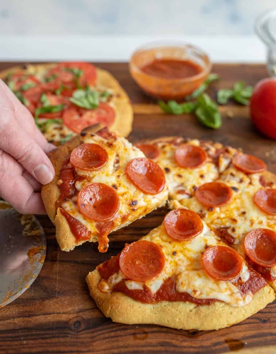A hand pulling a slice of gluten-free pepperoni pizza off the main pizza.