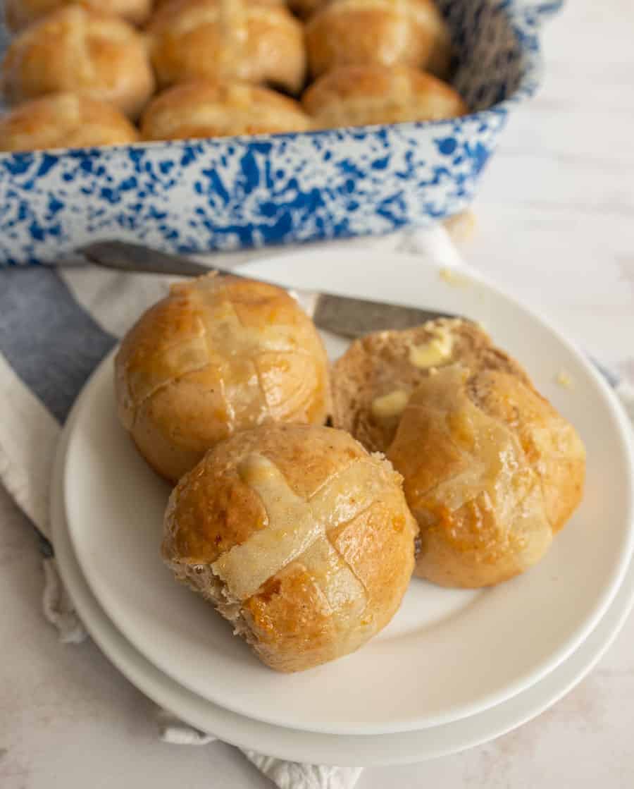 A close up of three hot cross buns on a white plate, one with a bite taken out of it.