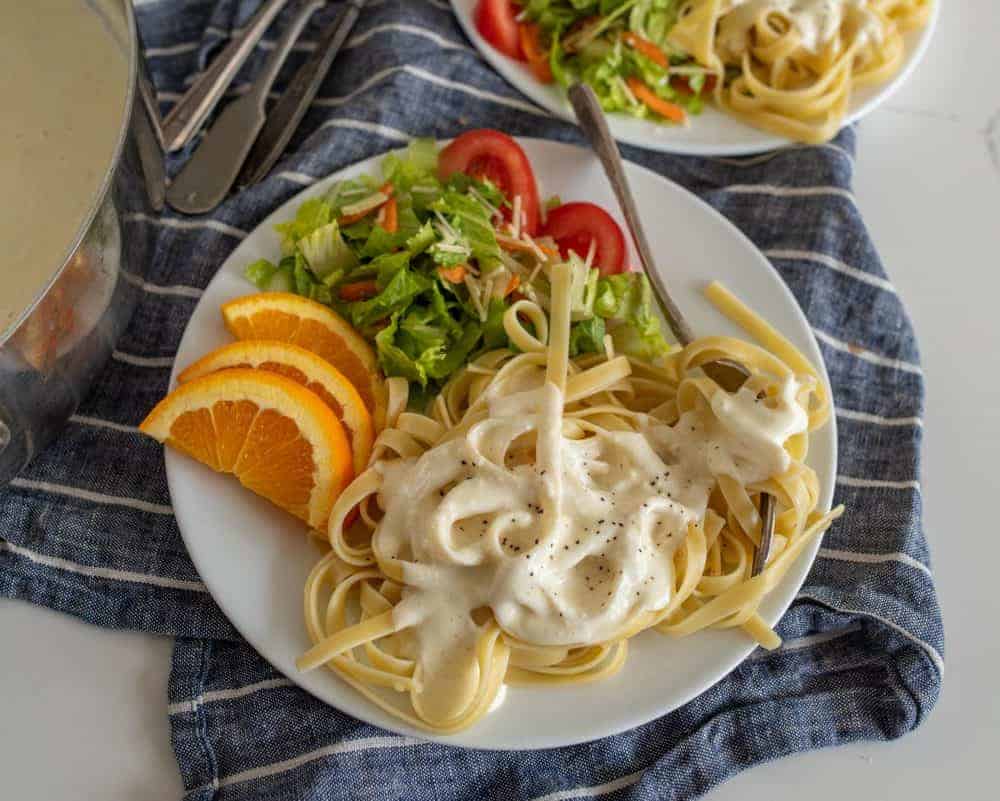 Up close picture of a plate of alfredo pasta with salad and orange slices.