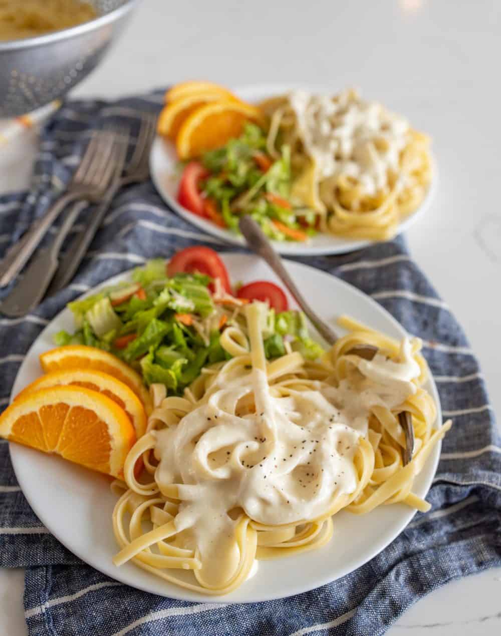 Plates of alfredo with salad and orange slices.