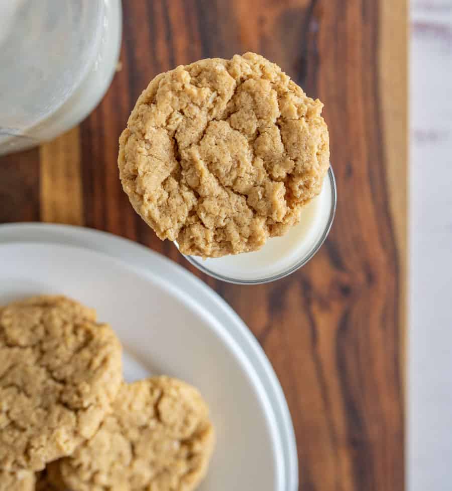 top view of an oatmeal peanut butter cookie on a glass of milk, next to a plate of cookies.