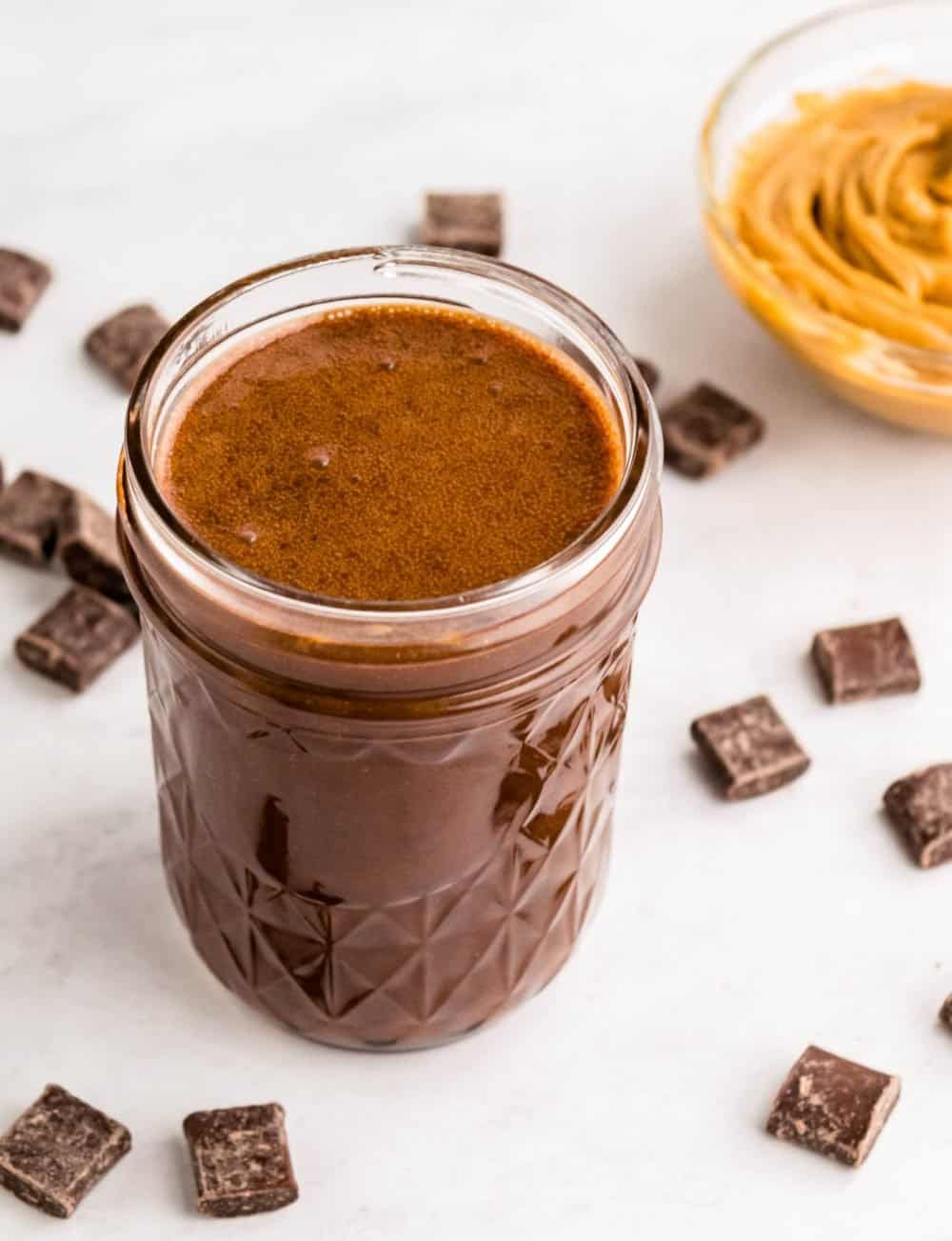 Top view of a jar of peanut butter hot fudge with a bowl of peanut butter and chocolate chunks surrounding it.