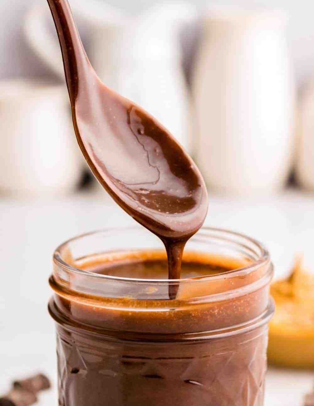 Close up picture of a spoon covered in peanut butter hot fudge over a jar of peanut butter hot fudge.