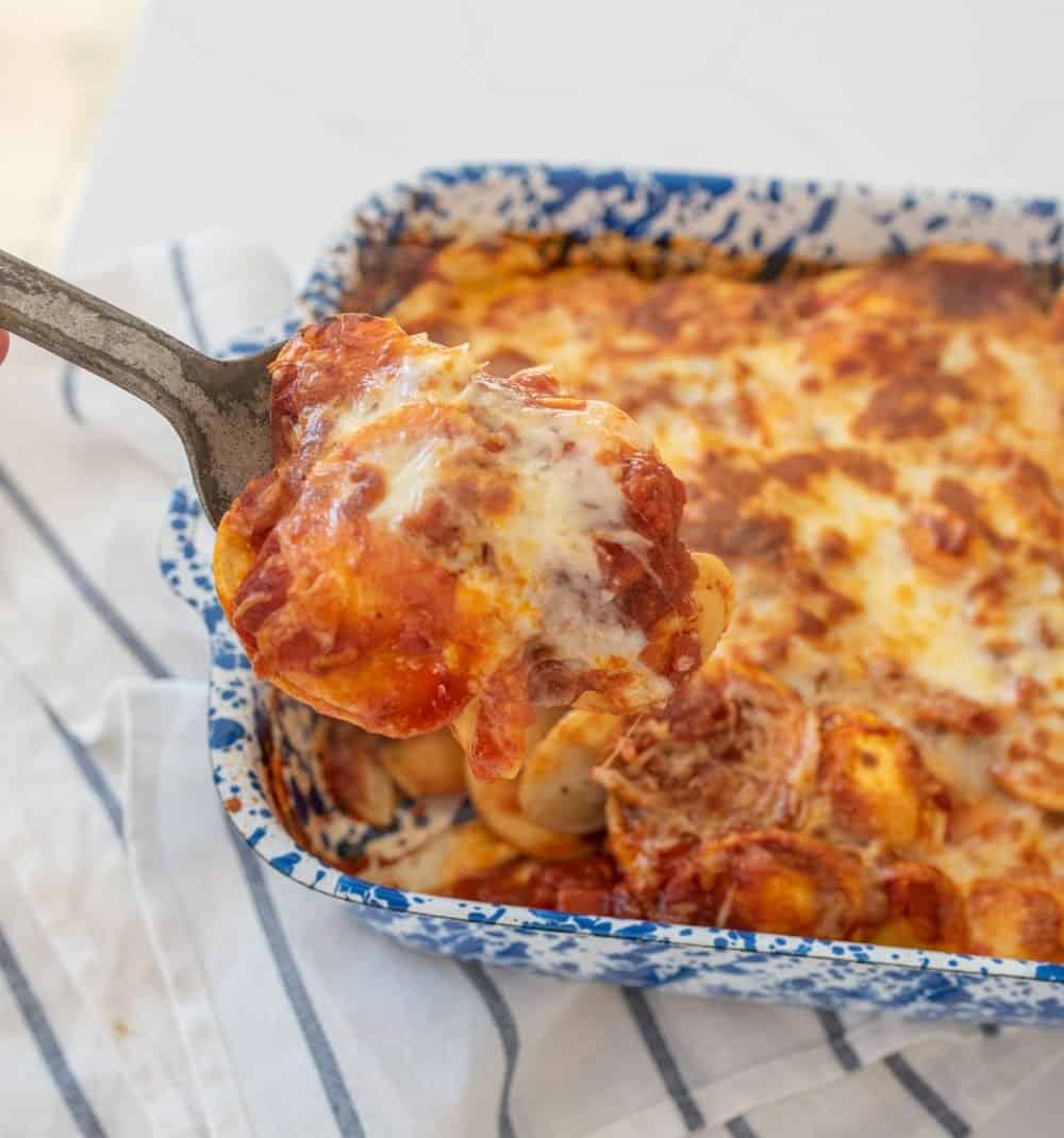 An up close shot of a spoon scooping ravioli lasagna from a baking dish.