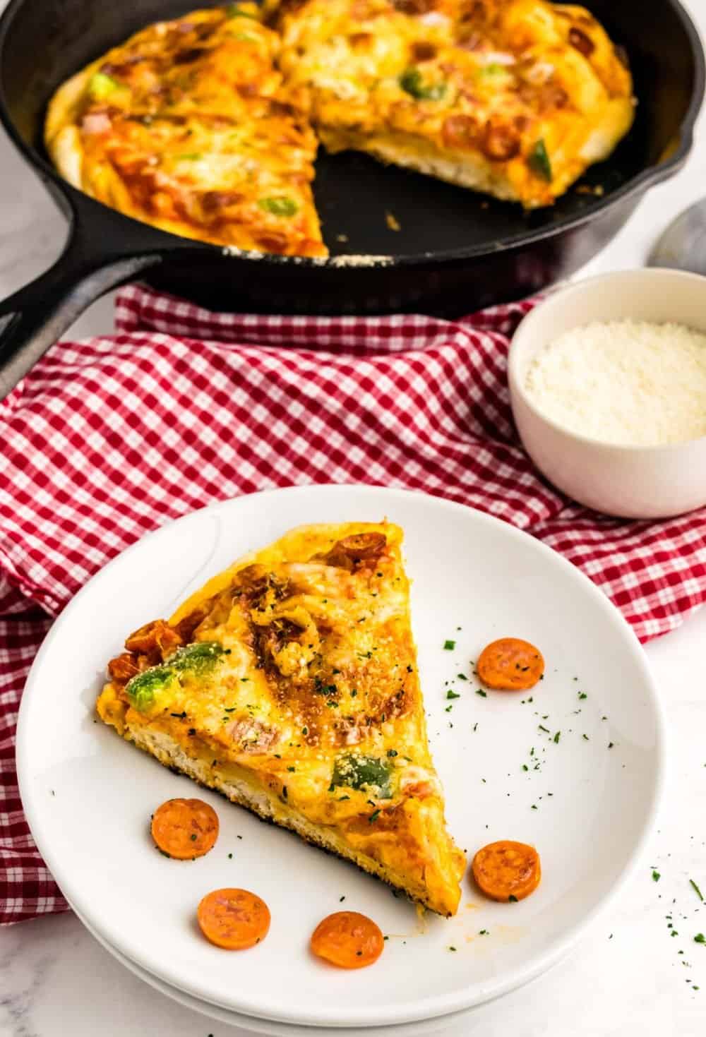 A slice of skillet pizza on a plate with pizza in the background.