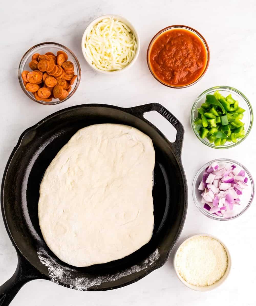 A top view of bowls of ingredients and dough in skillet for pizza.