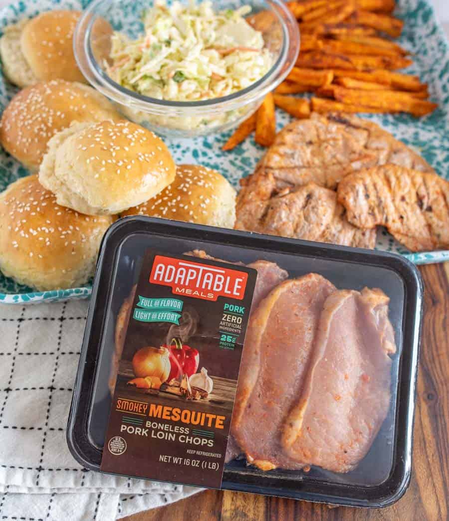 Package of unopened AdapTable meals Pork Loin Chops with grilled pork chops, buns, cole slaw and sweet potato fries in the background.