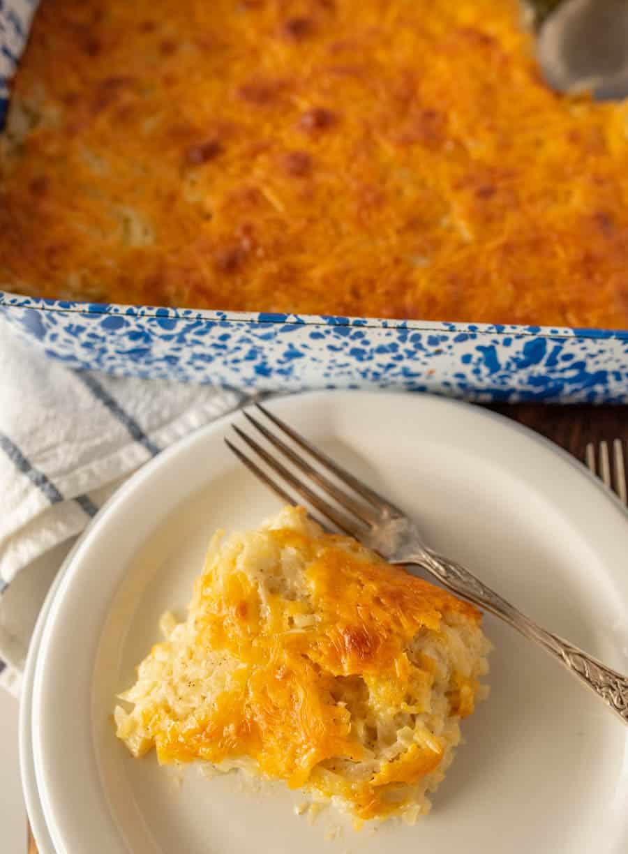 cheesy potato casserole on a plate with a fork and the baking dish in the back